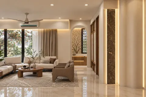 Living room, alcove side, Gulmohar House. Sheer curtains, a round walnut table, and a brown stone pilaster lit from both sides.